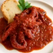 Polpo alla Luciana con sugo di pomodorini, olive e capperi servito in piatto con pane tostato