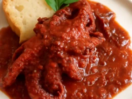 Polpo alla Luciana con sugo di pomodorini, olive e capperi servito in piatto con pane tostato