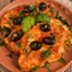 Petti di pollo alla mediterranea con sugo di pomodoro, olive nere fresche, capperi e foglie di basilico serviti su un piatto di terracotta.